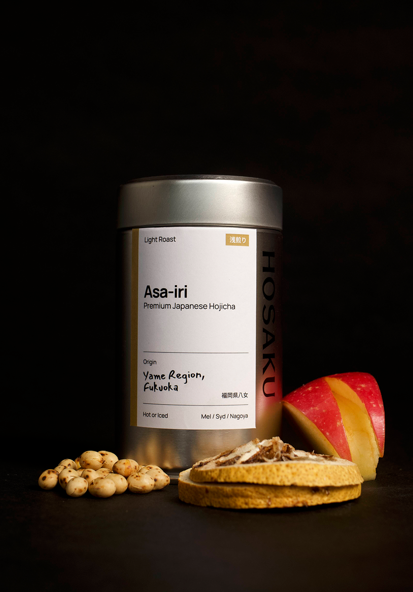 Hosaku Asa-iri Hojicha tea canister with cookies and a red apple on a dark background